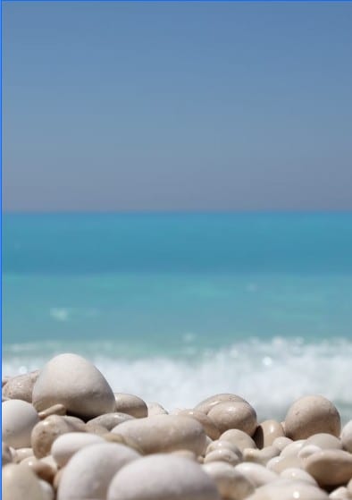 Smooth white pebbles on a Côte d'Azur beach with a turquoise sea in the background