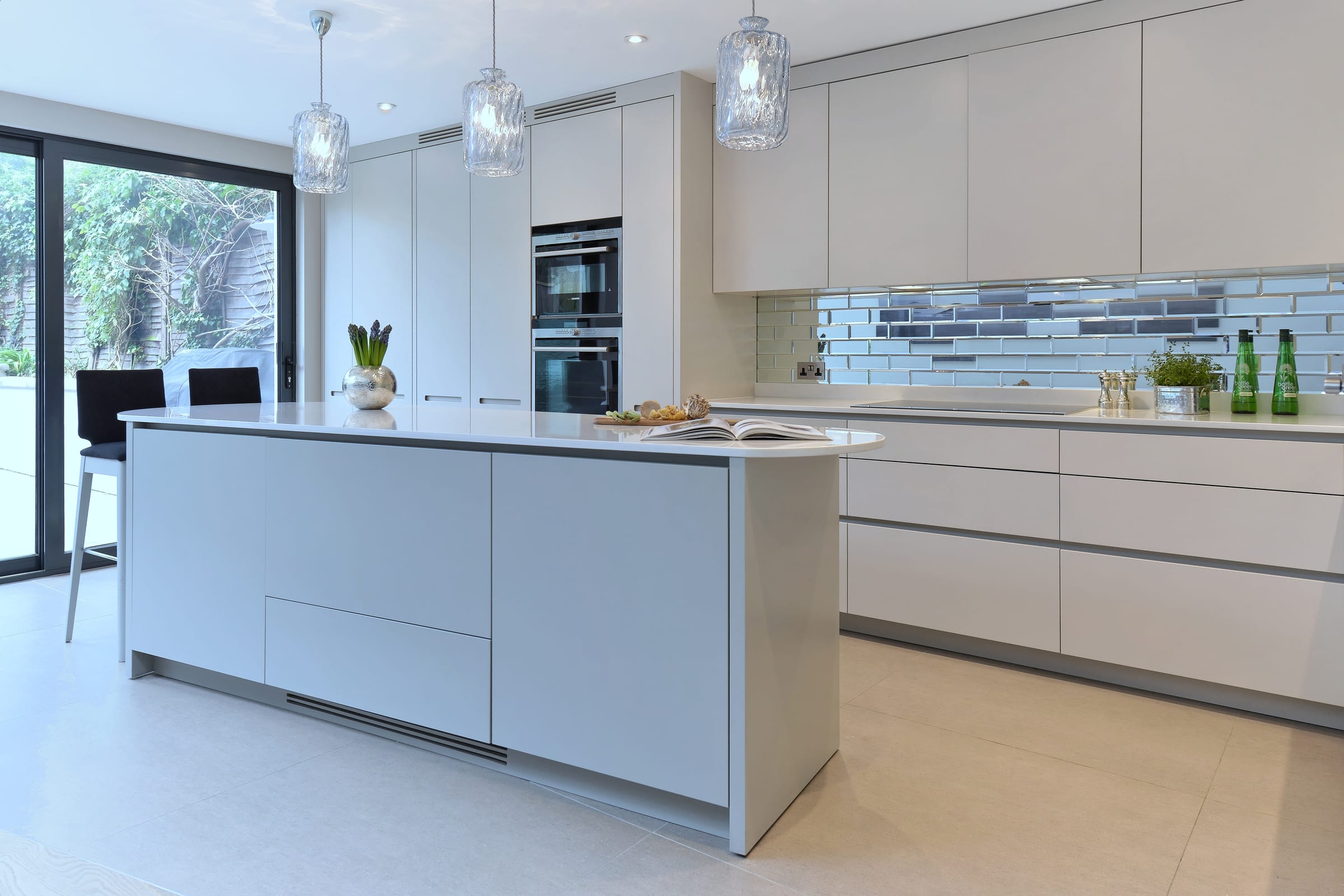 Beige bespoke kitchen in Balham with asymmetrical island and mirrored backsplash