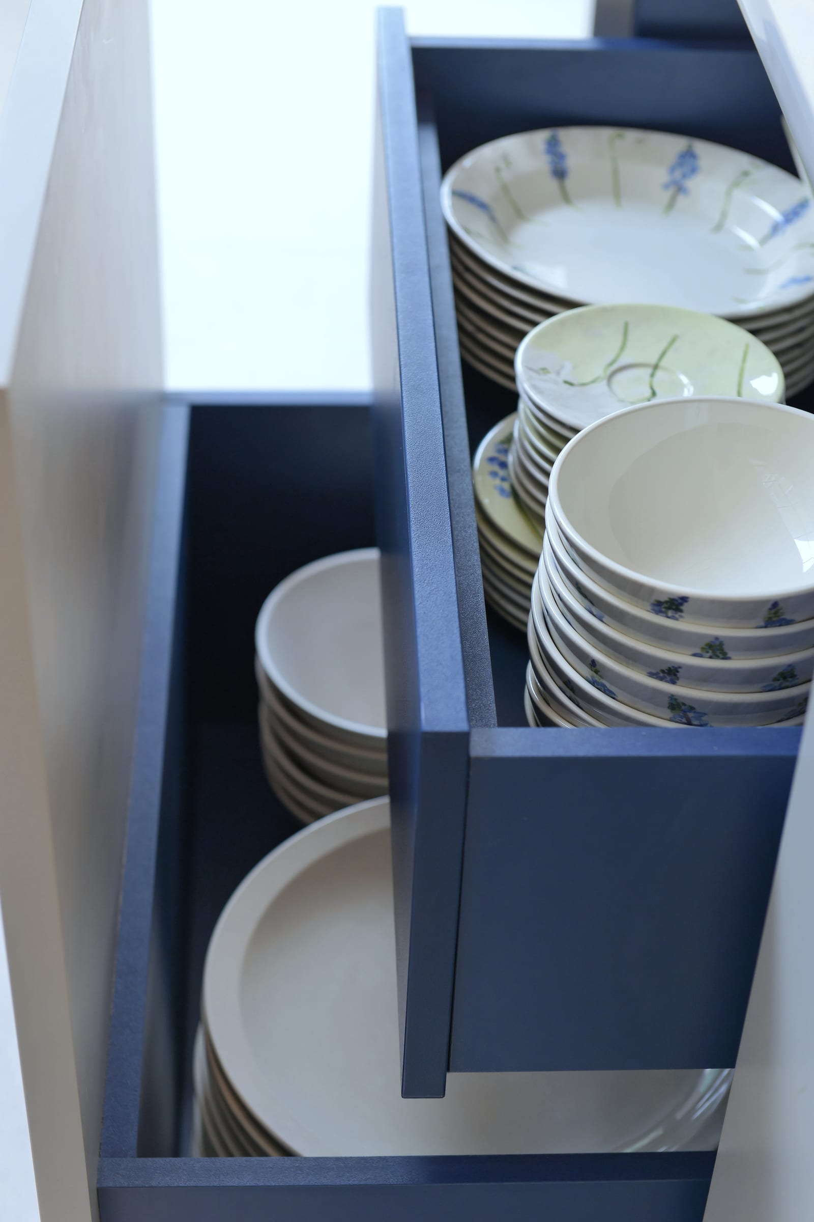Navy-blue drawer organiser with stacked patterned bowls and plates