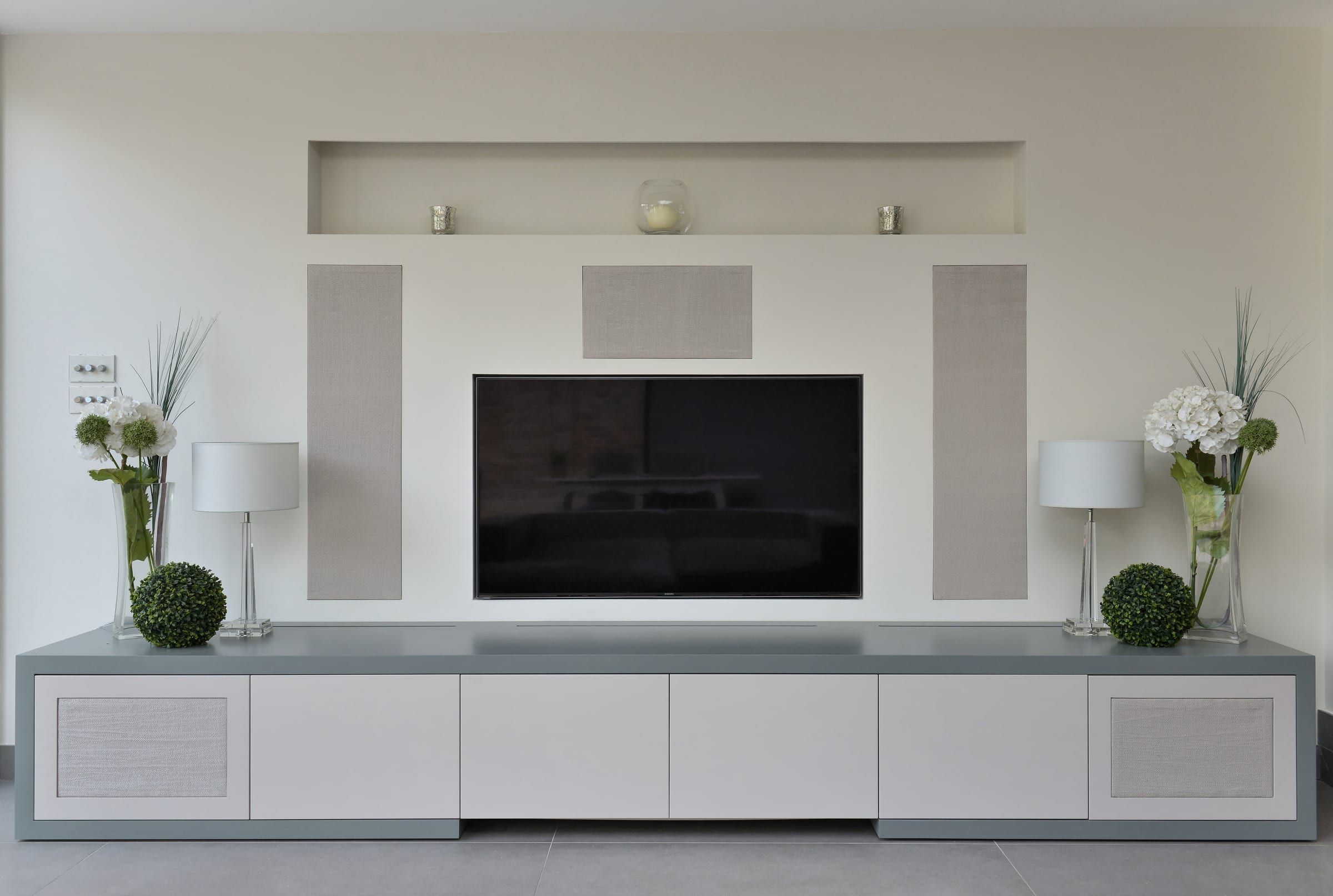 Fabric-inlay cabinet door concealing a wall-mounted speaker, part of a bespoke home cinema unit in Richmond
