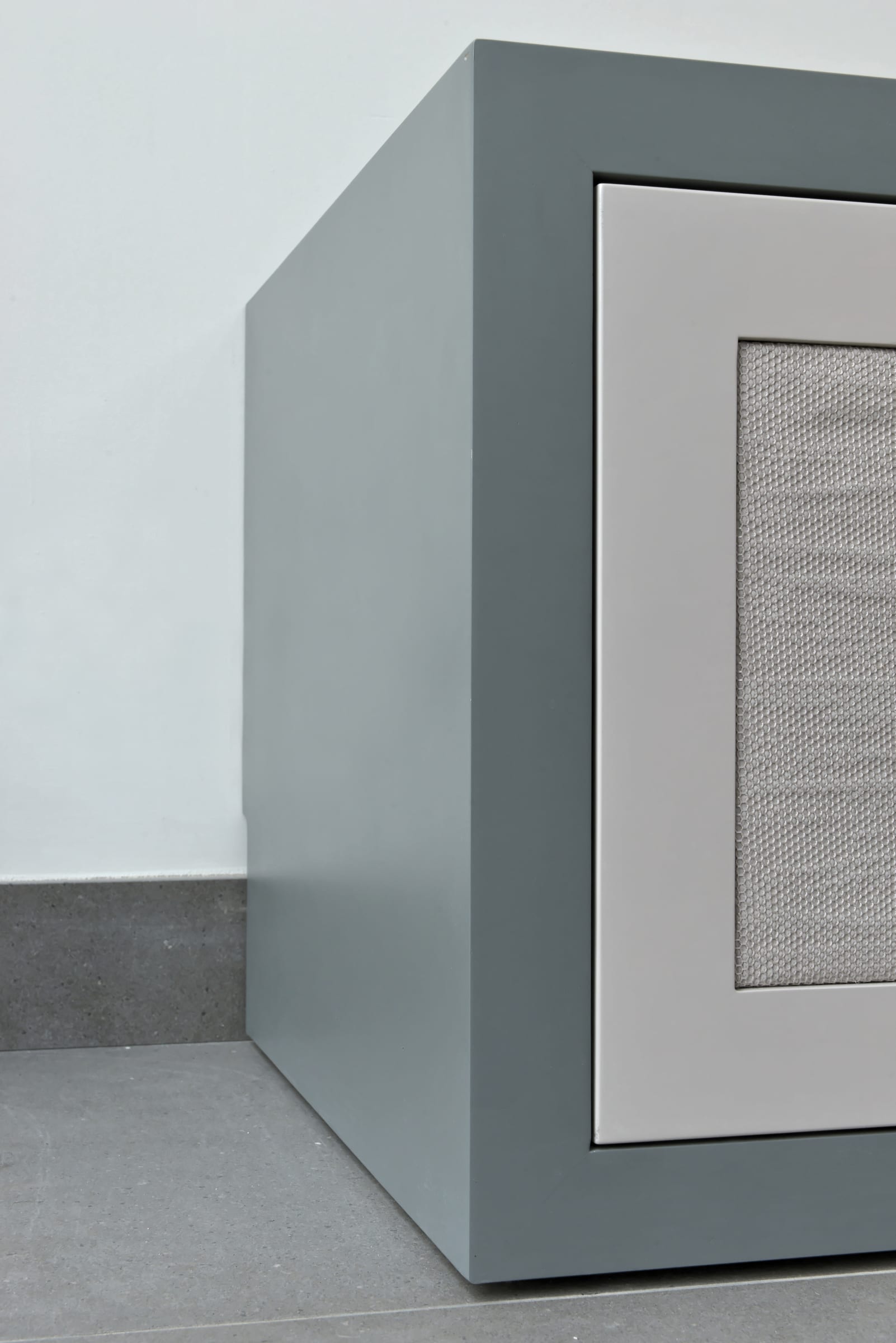 Corner detail of a fabric-inlay cabinet door concealing a speaker, in soft grey-blue joinery
