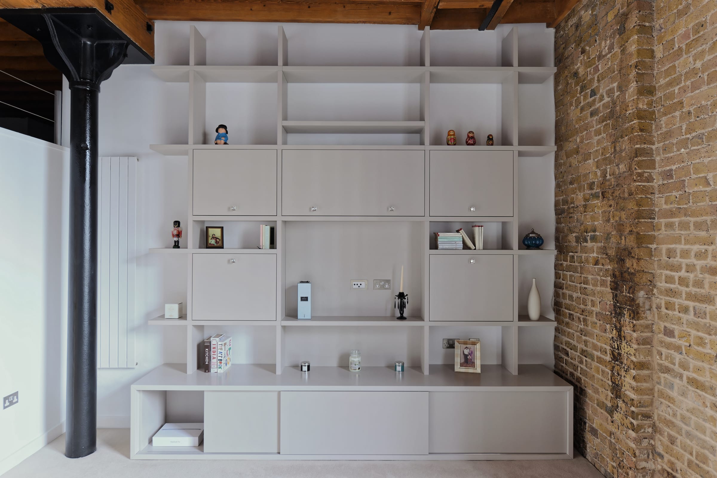 Bespoke shelving and bar joinery styled with books and glassware against an exposed-brick wall in an East London loft