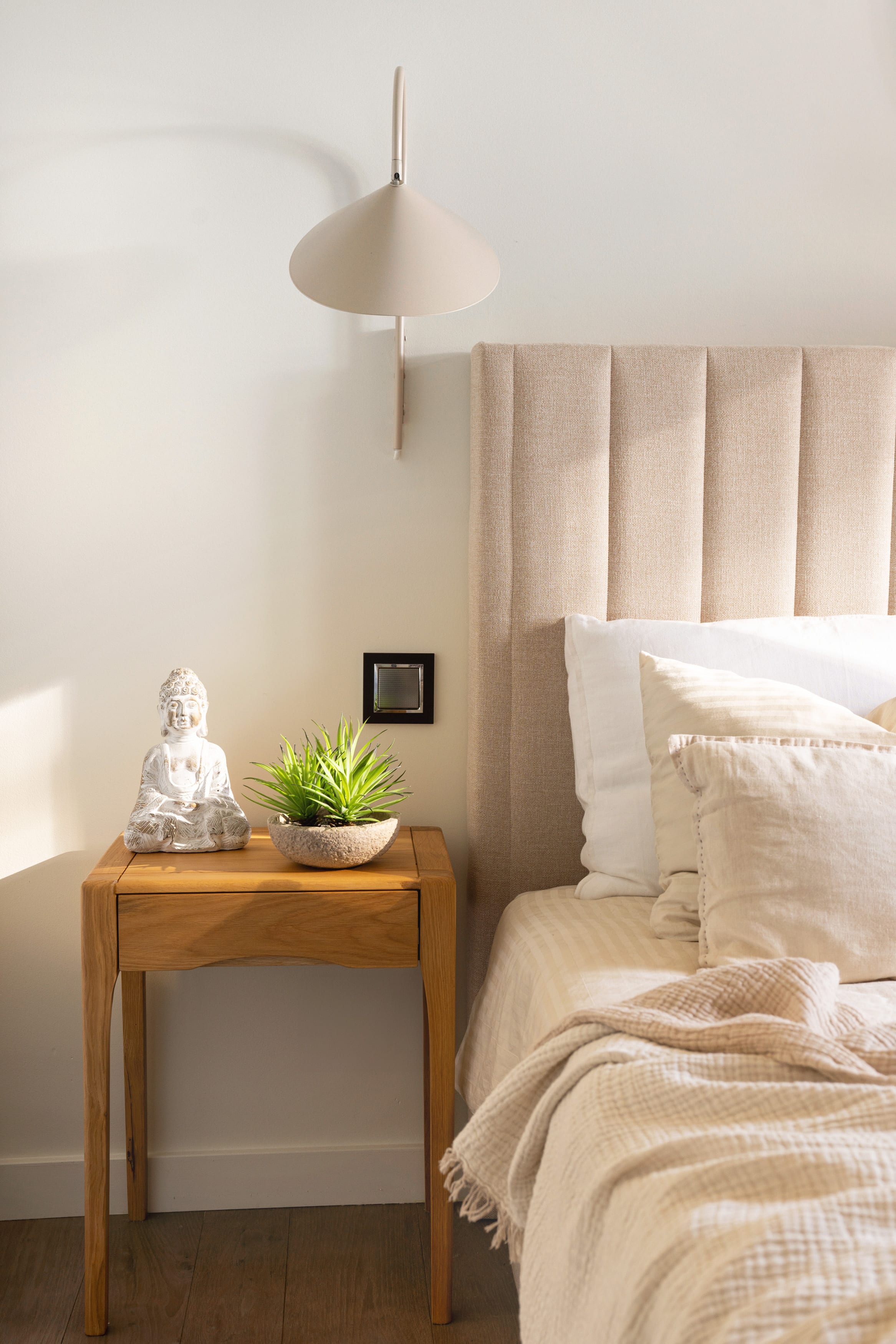 Bedside detail with a stone Buddha figurine, a small potted plant, and a channel-tufted headboard