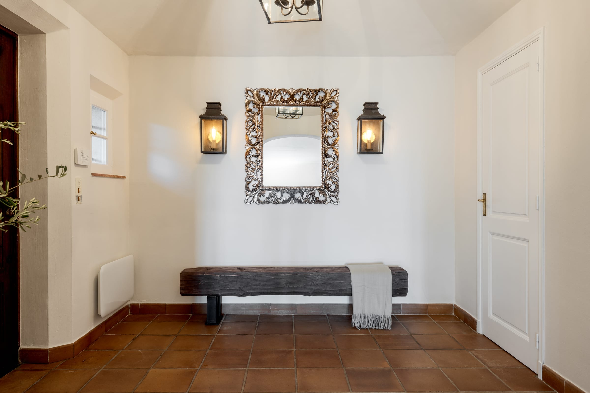 Entryway with an ornate gilt mirror, wall lanterns, and a reclaimed-wood bench